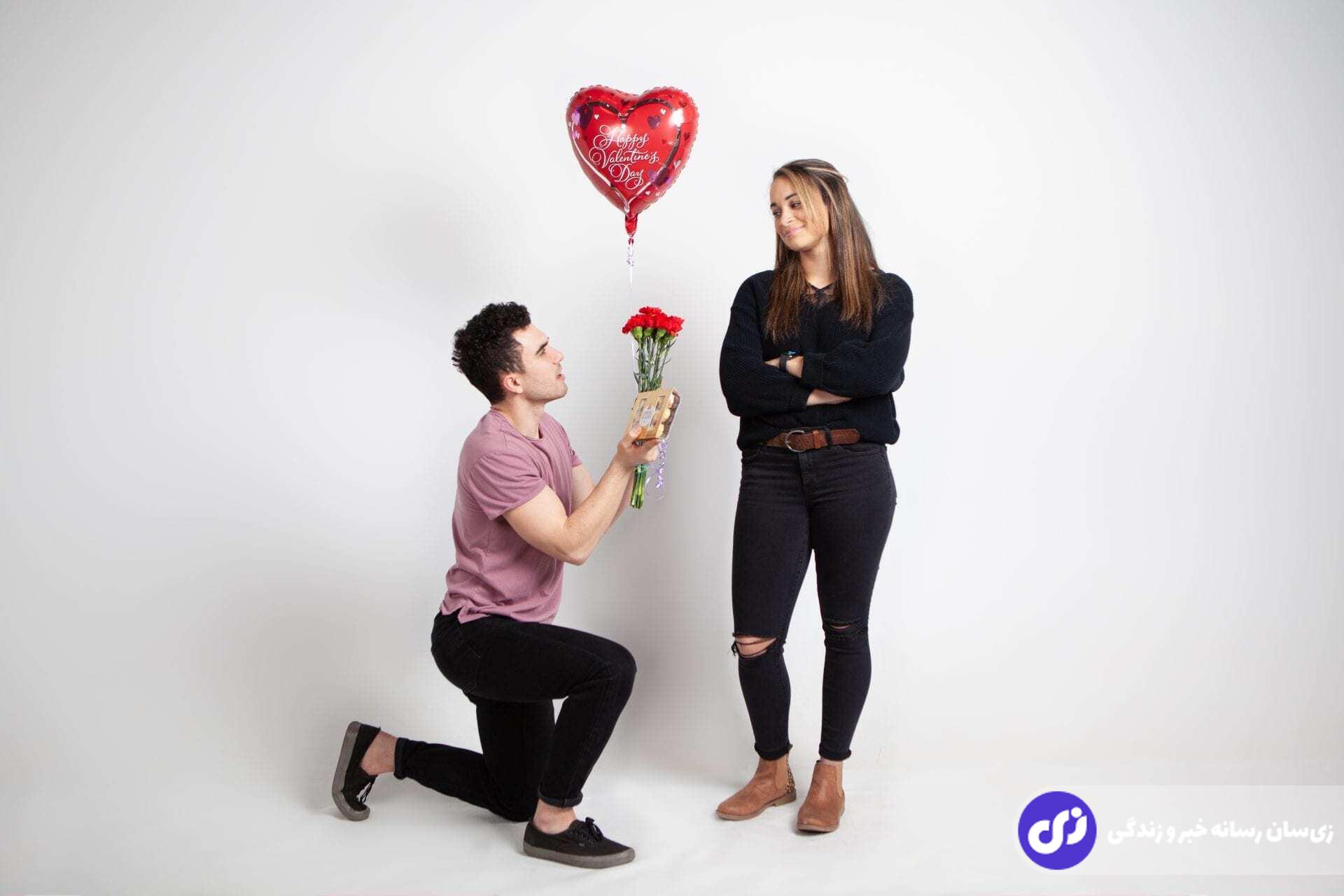 مردی زانو زده و یک هدیه و بادبادکی به شکل قلب را در روز ولنتاین به دختری هدیه می دهد