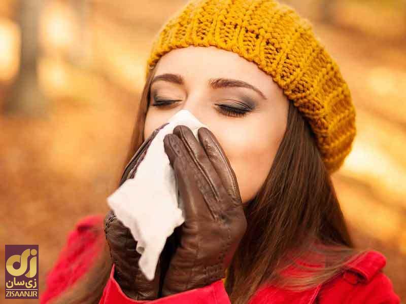 زنی در حال عطسه کردن با کلاه زرد رنگ بافتنی و لباس قرمز در فصل پاییز